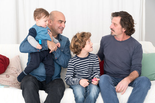 Happy Gay Men Posing Sitting On The Sofa With Their Two Children