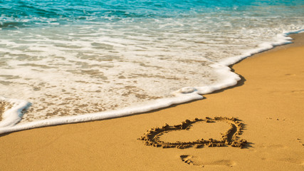 Drawing a heart on the beach sand on the beach with sea waves in the background. Selective focus. Beautiful deserted beach. Trace of human foot on the sand.