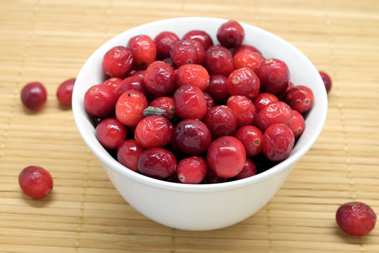 Cranberries in round white bowl and scattered blueberries on brown straw mat top view