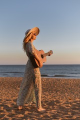 Beautiful woman playing guitar on the beach at sunset outdoors background