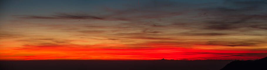 Fiery sunset from mountain pick with thin glazes in the sky evening. Fall season. Orobie alps. Rena pick. Bergamo Italy. In the distance the Monviso.