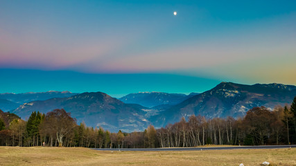 Colorful scenery with autumn trees and moon over mountain range