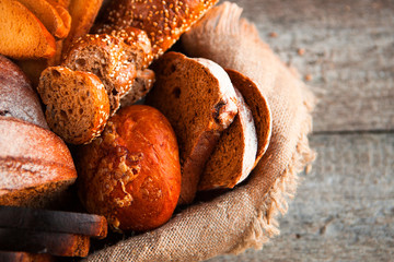 Different fresh bread in wicker basket on rustic table on wooden