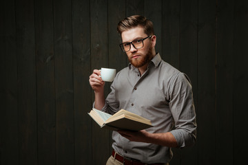 Portrait of concentrated man holding open book and drinking coffee