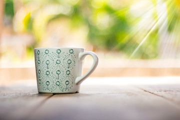 White cup with green pattern on wooden background