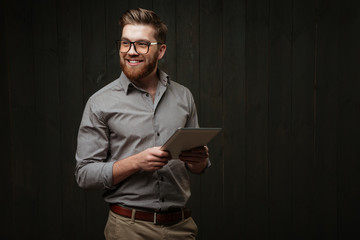Smiling man in eyeglasses holding tablet computer and looking away