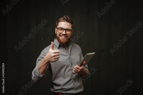 "Smiling handsome young man using tablet and showing thumb