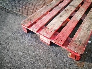 Alte Palette aus Holz mit roter Farbe und Riffelblech auf grauem Asphalt im Sonnenschein vor einer...