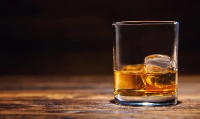 Fotobehang Alcohol Glas whisky met ijsblokjes geserveerd op hout