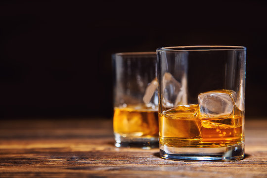 Glasses of whiskey with ice cubes served on wood