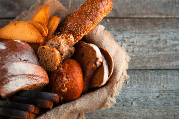 Different fresh bread in wicker basket on rustic table on wooden