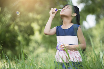 Cute little girl wearing a blue and white dress blowing bubbles in the park,vintage style.