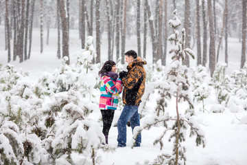 Fototapeta na wymiar Winter couple in love, young couple in colorful winter jackets looking at each other in snowy winter forest