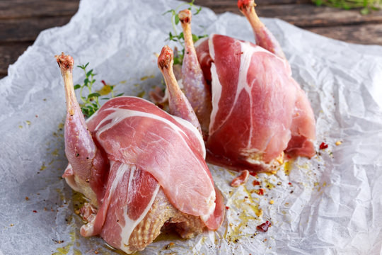 Ready to cook raw seasoned partridges with bacon on crumpled paper.