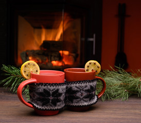 Cup with Christmas ornament near fireplace. Mug in knitted cloth