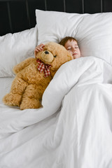 Cute boy sleeping with teddy bear in bed.