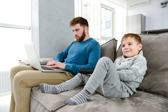 Young father using laptop while his son watching TV.