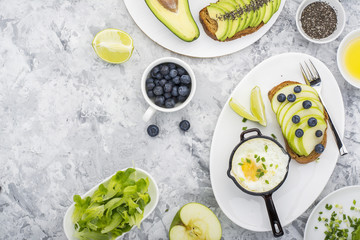 Healthy delicious breakfast of fried eggs in a batch frying pan and toast with green apple  avocado  blueberries on  marble background. Color year. Greenery. Top view
