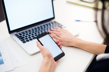 Woman's hands using mobile phone and laptop at the office