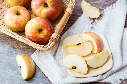 Дольки яблок на тарелке и целые яблоки в корзине, салфетка на деревянном столе 