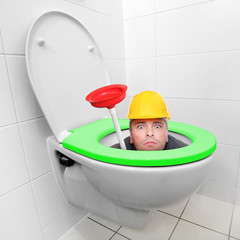 Funny repairman looking from toilet bowl with green seat in a modern bathroom. 