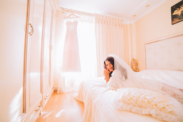 Obraz na płótnie Canvas Portrait of beautiful bride. Morning of the bride. Posing on the bed on the wedding morning. Makeup. Brunette girl with long wavy hair.