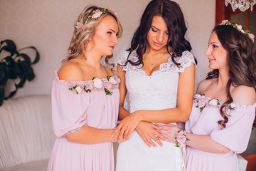 Beautiful blonde bride in luxury wedding dress and pretty twins bridesmaids in similar dresses in a morning. Fashion modern wedding photo