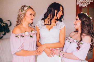 Beautiful blonde bride in luxury wedding dress and pretty twins bridesmaids in similar dresses in a morning. Fashion modern wedding photo