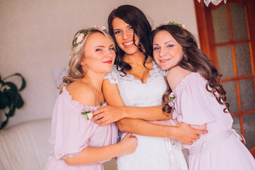 Beautiful blonde bride in luxury wedding dress and pretty twins bridesmaids in similar dresses in a morning. Fashion modern wedding photo