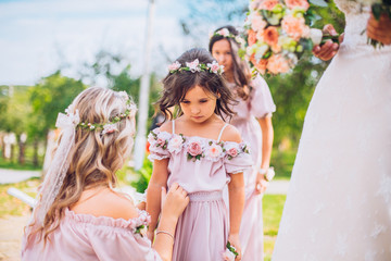Bride with bridesmaids and little girl kids in the same color dress posing on camera in the park on...