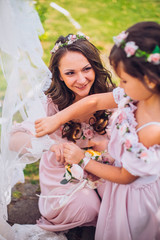 Fototapeta premium Bride with bridesmaids and little girl kids in the same color dress posing on camera in the park on the wedding day