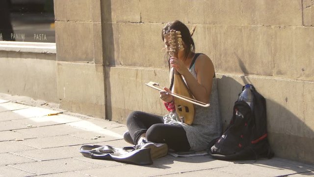 young street artist woman playing an old string instrument on the sidewalk 