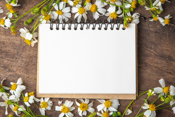 Blank notebook with white flower and bas ket of flower on vintage wooden table View from above with...