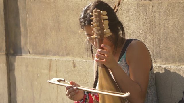 homeless young woman playing music instrument on the sidewalk 