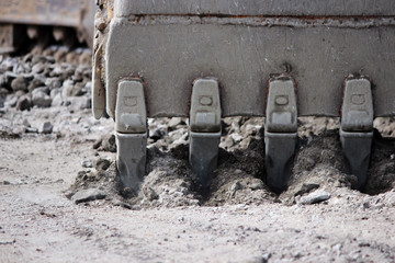 Excavator bucket digging a trench at the side of the road for its expansion.