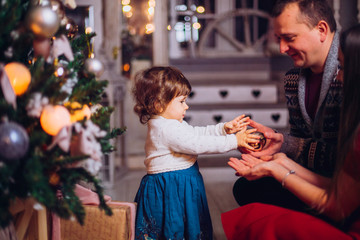 Portrait of affectionate family in christmas time. Family (mother, father, and little cute daughter) sitting near a Christmas tree and smiling face in the frame