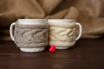Obraz na płótnie Canvas Cups of coffee with knitted cup holder near heart - symbolizing love of coffee