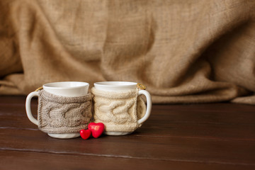 Fototapeta na wymiar Cups of coffee with knitted cup holder near heart for valentine's day. Love coffee