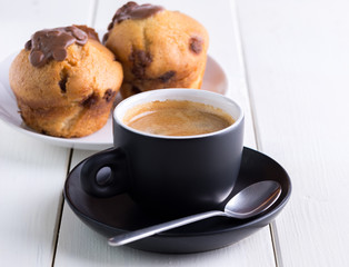 Morning coffee in black cup on white natural background with muffin behind.