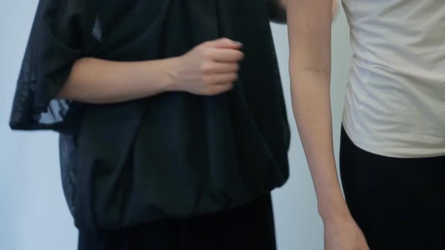 Two women stand in front of mirror and examine figure of one of them.