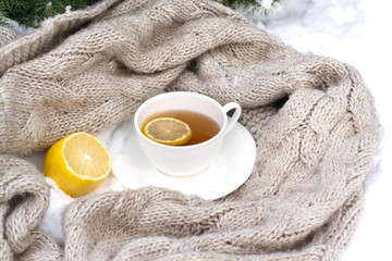 white mug of tea wrapped in a knitted scarf on a saucer, lemon i