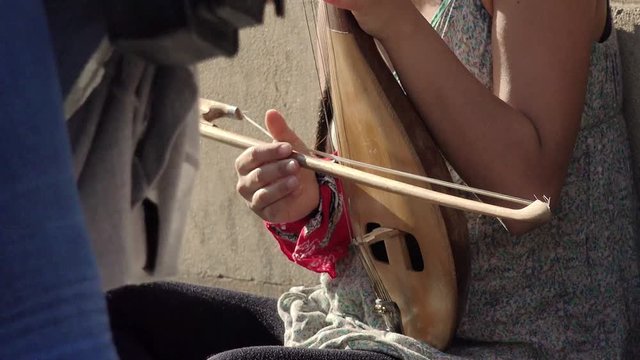woman playing an ancient stringed instrument on the street sitting on sidewalks