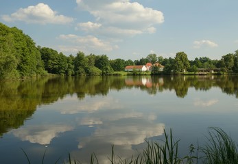 Pond on whose surface mirrors the sky and on the shore the farmhouse and chapel.