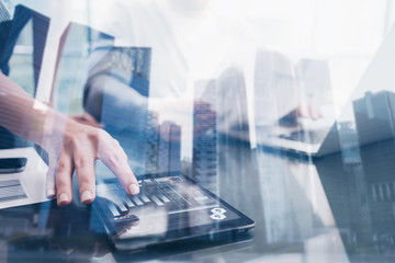 Closeup female hand touching tablet display in coworking place.Concept of business people using mobile divece.Icon and graphs on screen.Double exposure,skyscraper office building blurred background.