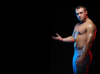 male bodybuilder athlete with naked torso posing against a black background, in red and blue light