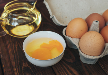 broken egg in a bowl, eggs and sunflower oil in a glass container 
