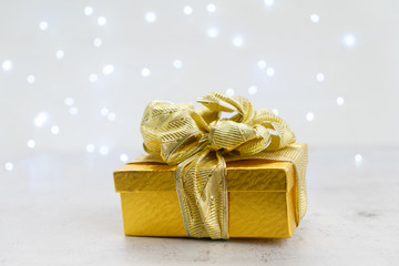 Christmas golden present box with bow, bokeh lights in background