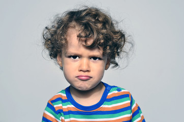 Beautiful curly toddler looking angry, sad boy being naughty