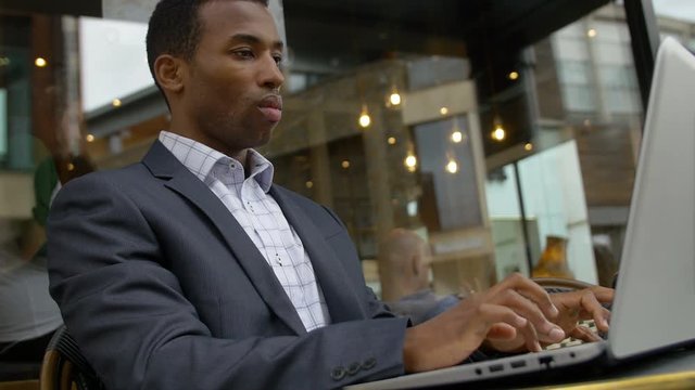 black businessman working with laptop in a cafe: cafeteria, outdoor 