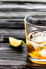 rum with ice in glass on dark background and lime